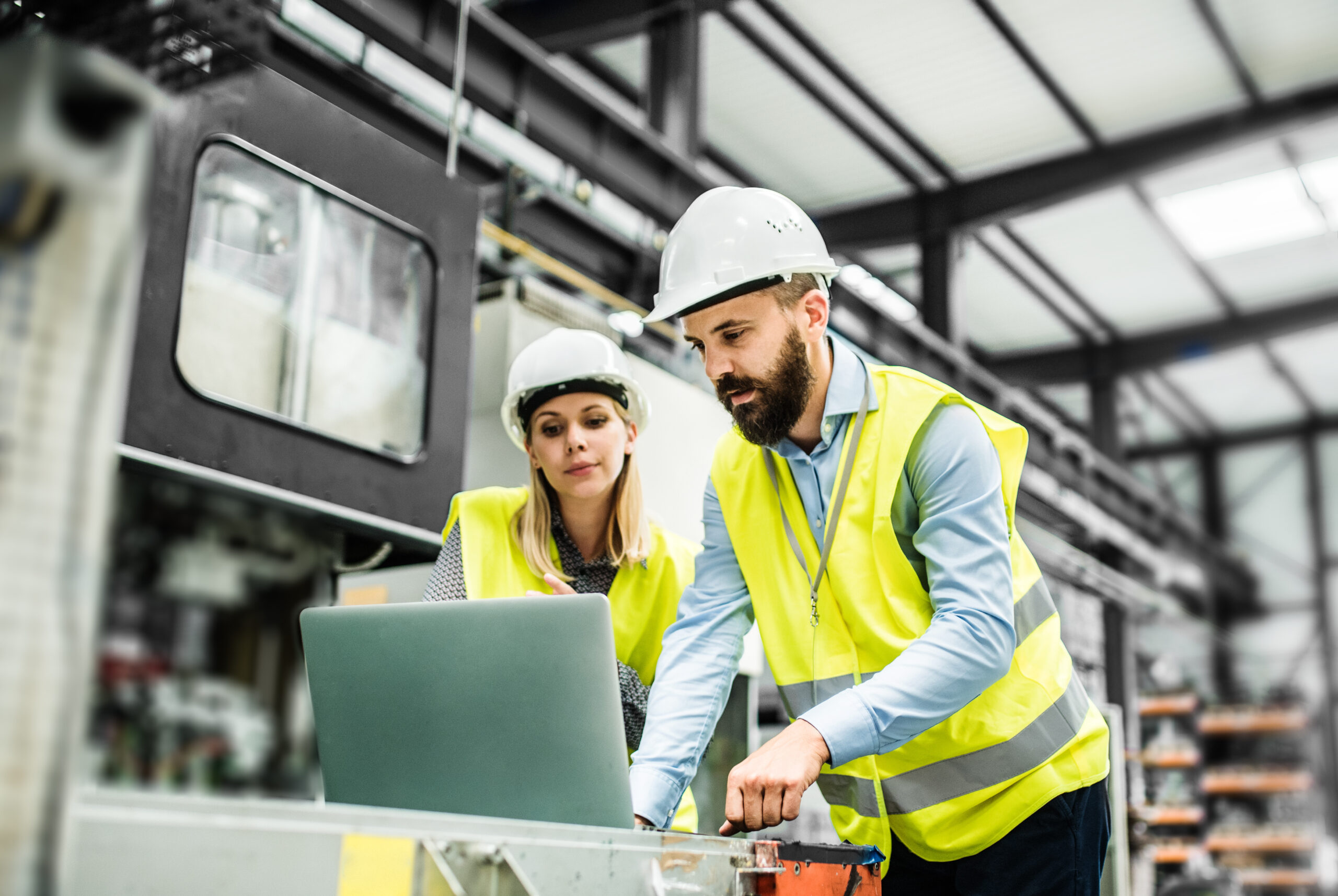 Two computer system validation engineers reviewing qualification documentation on a laptop in a pharmaceutical manufacturing facility.