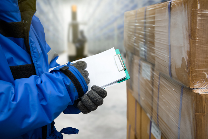 hand of worker with clipboard checking goods in freezing room or warehouse